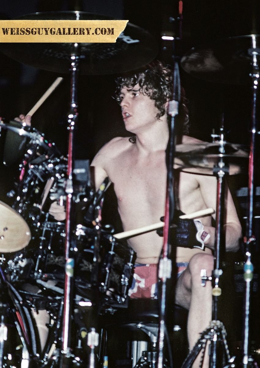 Rick Allen drummer of Def Leppard Pyromania Tour 83- When I first started playing with Rick I thought he was using a double kick drum. But he had this amazing technique where he would flick his heel on the pedal and make it sound like a double kick. Ricks technique was pretty grownup for a rock drummer as he used jazz techniques and he was so young. I remember once on this tour we went to jam with a band at the hotel we were staying at but Rick wasnt allowed in because he was under aged.  This was to be Ricks last tour with this way of playing. The next year on New Years Eve he had a horrific car crash that severed his left arm. This actually led to a period of total inspiration for him and everyone who was around to witness. When Steve and I visited him in the hospital he told us hed been practicing on the pillows in his bed and that he was going to replace his lost left arm with his left leg and a series of pedals that would allow him to continue drumming. The result was astounding. He would get up at 8am every morning and play til nightfall every single day. He not only dealt with the frustration of learning a new way to play drums but then there was the everyday life stuff ie., tying shoelaces and even standing up straight. Rick pulled this off big time with humility and humor. He continues to be a huge inspiration to me, the band, and many others.